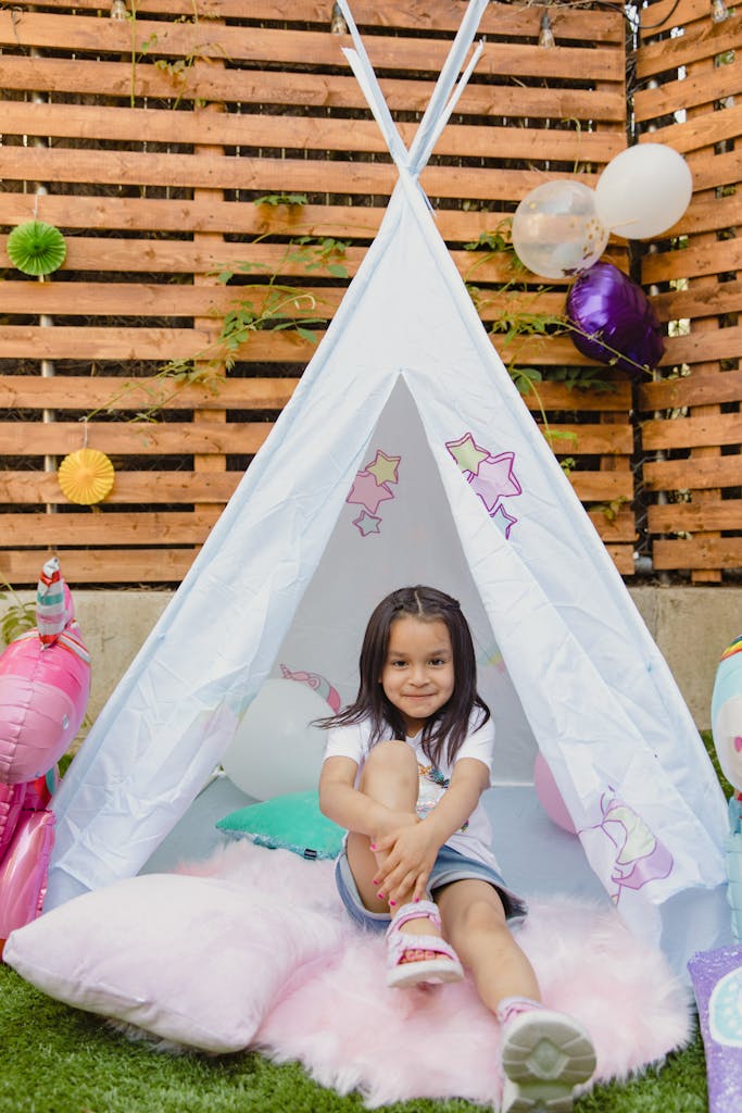 A young girl enjoys a whimsical outdoor play setting with colorful balloons and a teepee tent.