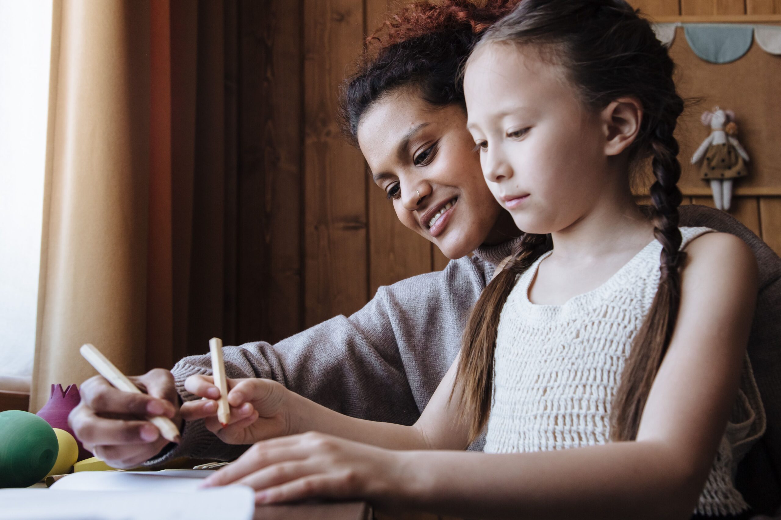 Mother and daughter drawing together with coloured pencils at home.